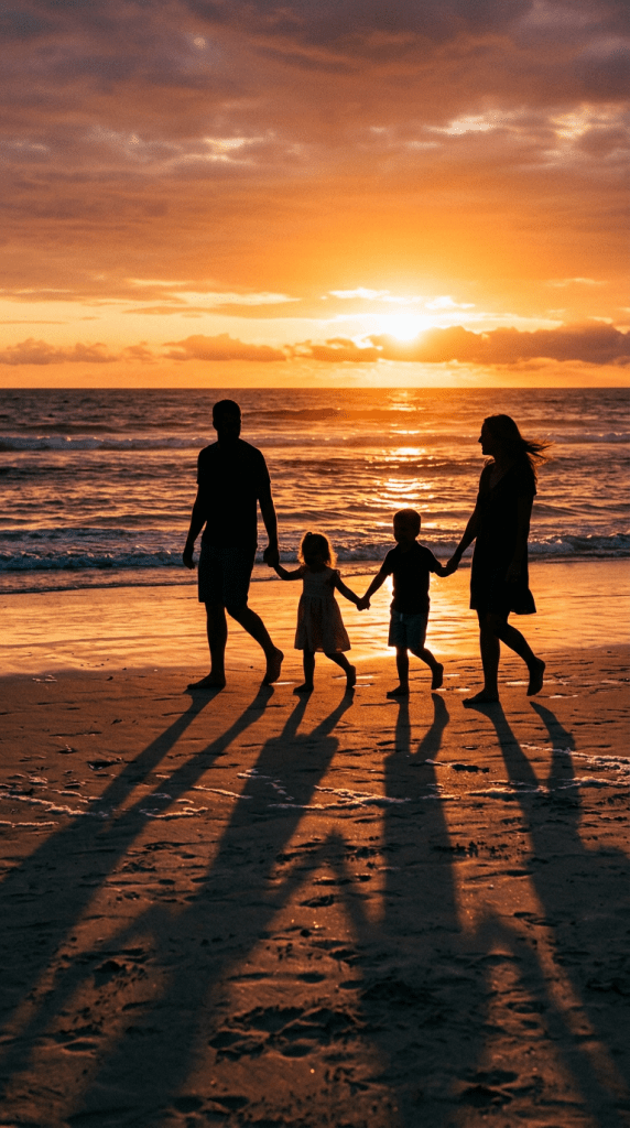 Silhouettes of two adults and two children holding hands walking on the beach at sunset